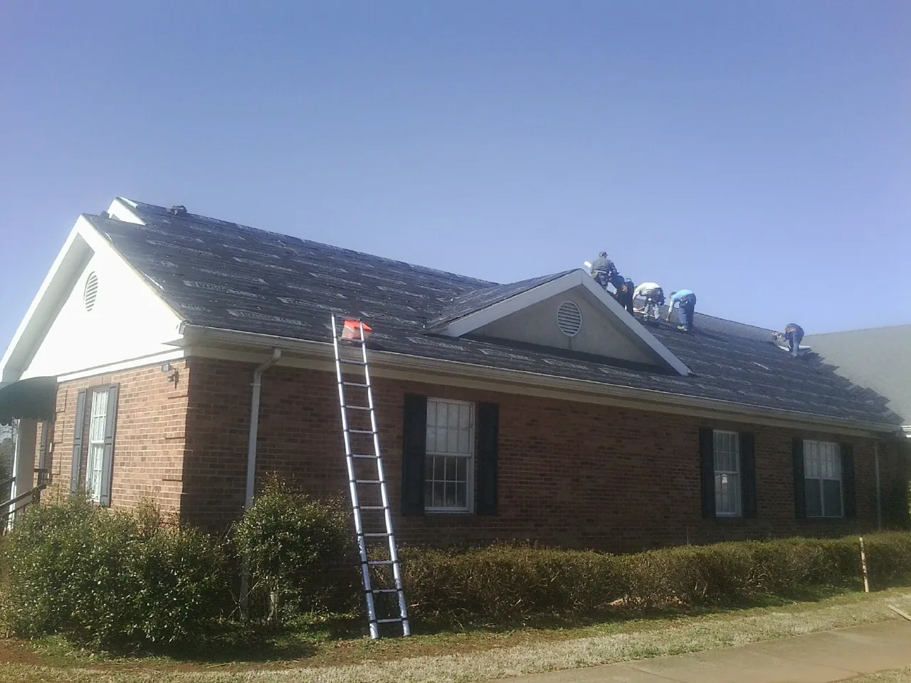 Crew tearing shingles off a brick ranch roof with a ladder set — Metal Roof Repair work by our crew in Somonauk