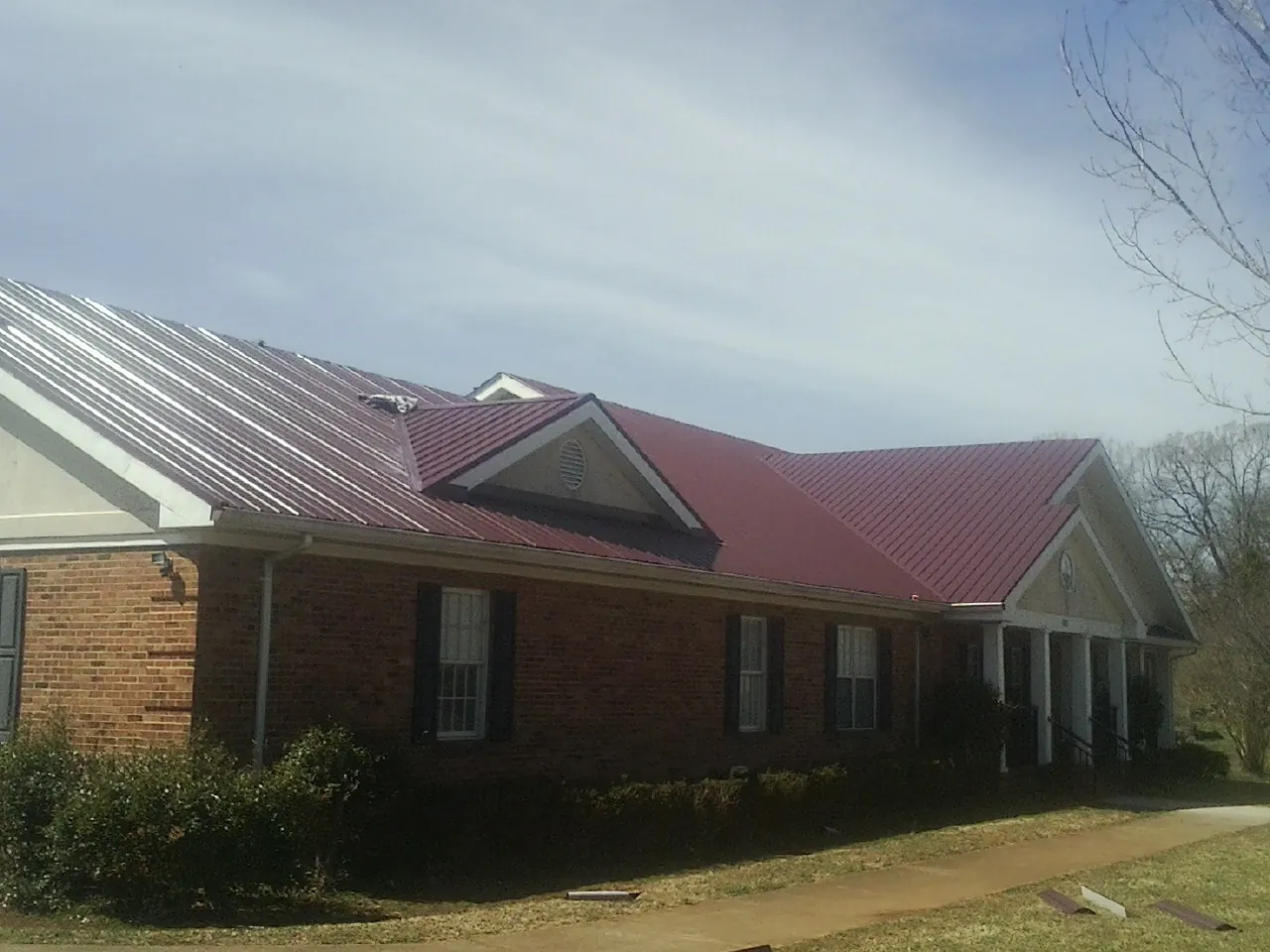 Red metal roof with gabled entries on a long brick building, from a Hail Damage Roof Repair job in Somonauk