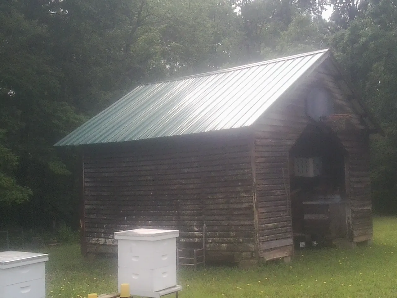 Green metal roof on a weathered barn beside stacked beehives in Somonauk