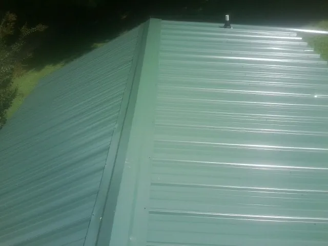 New green metal panels meeting at the ridge of a roof — Flat Roof Repair work by our crew in Somonauk