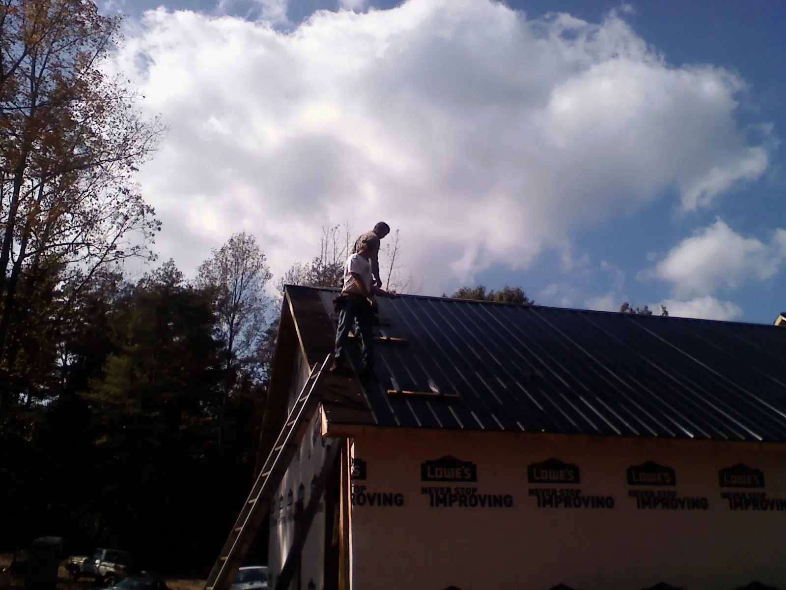 Roofer fastening dark metal panels high against a cloudy sky, from a Roof Inspection job in Somonauk