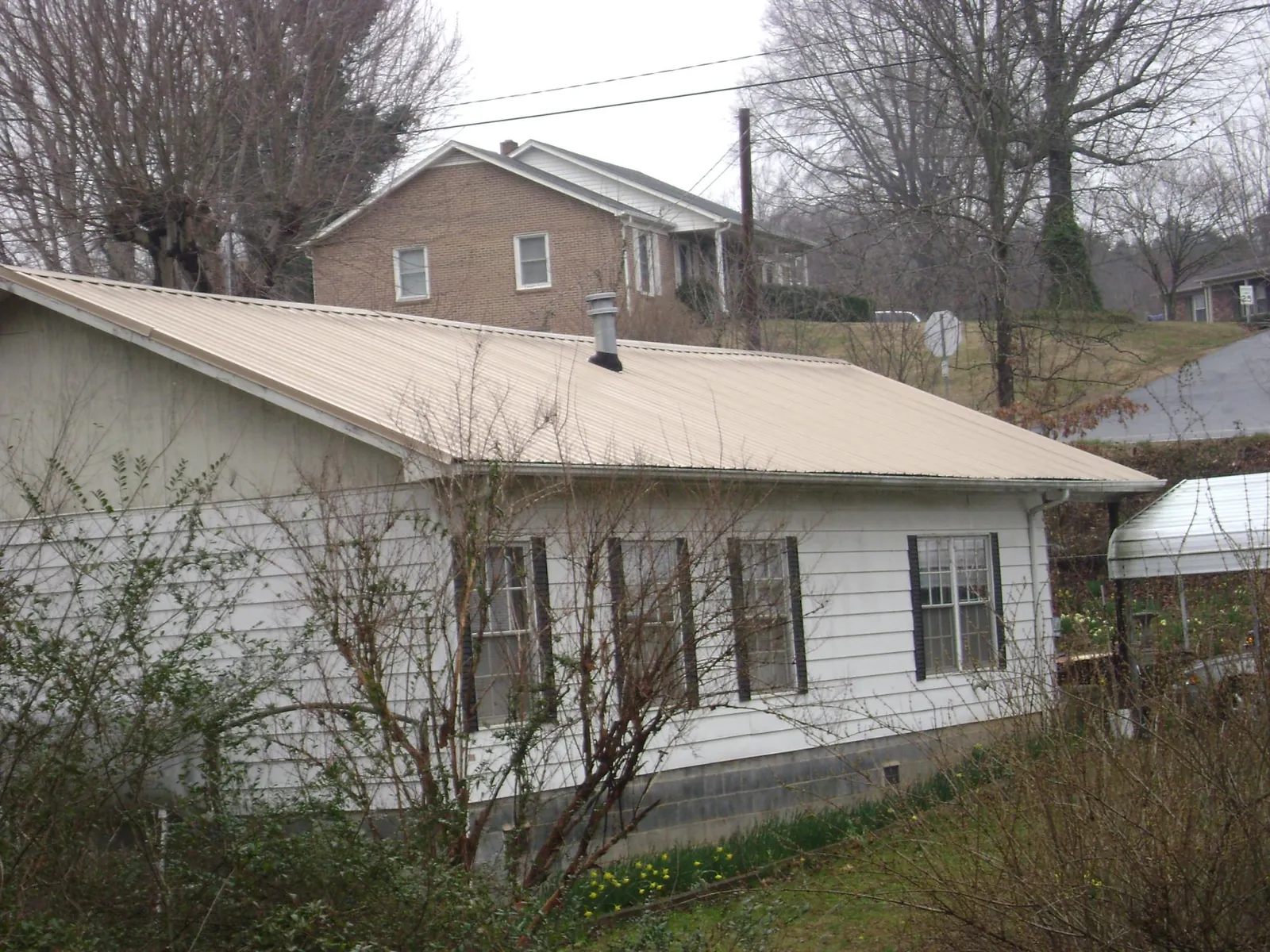 Tan metal roof on a white sided house set into a hillside — Commercial Roofing by Roofing Brothers in Somonauk